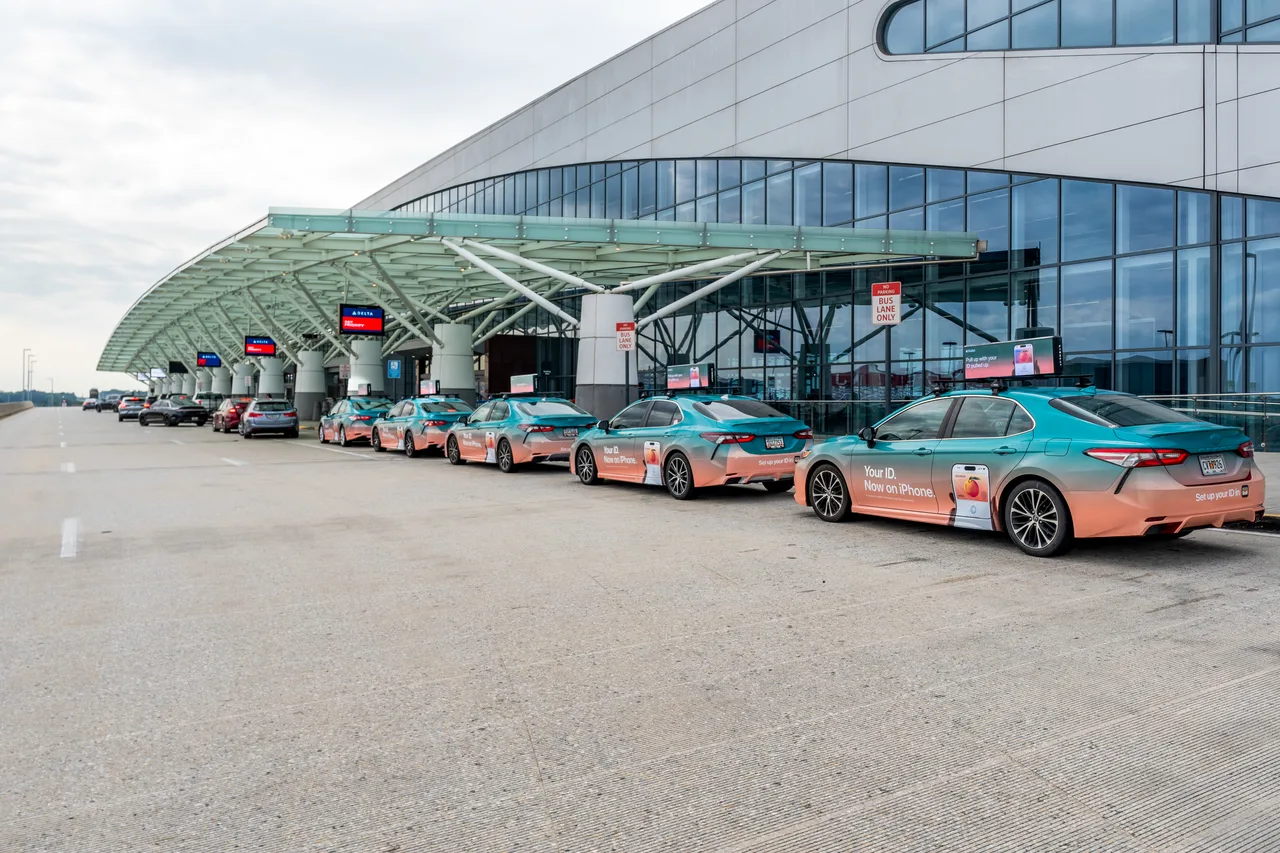 Apple campaign on a swarm of wrapped cars with digital tops at Hartsfield-Jackson international terminal curb, Atlanta, 2024