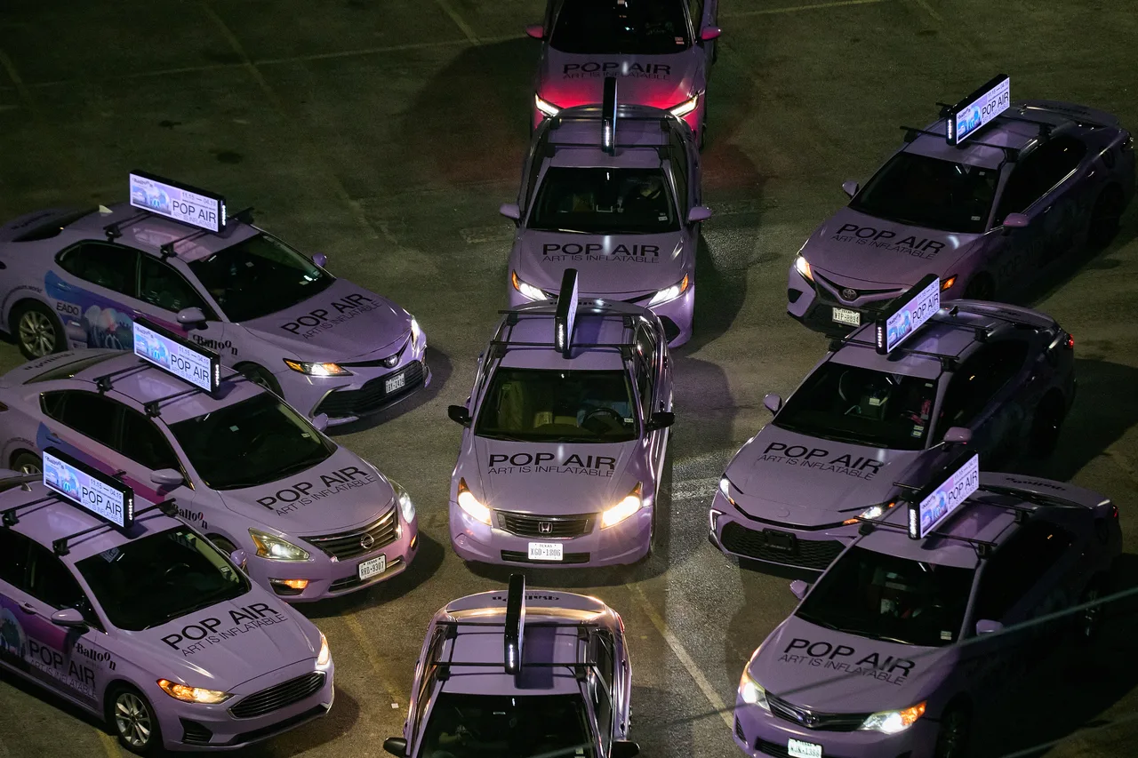 Balloon Museum campaign on a swarm of wrapped cars with digital tops at ten-car swarm at night, Houston, 2025