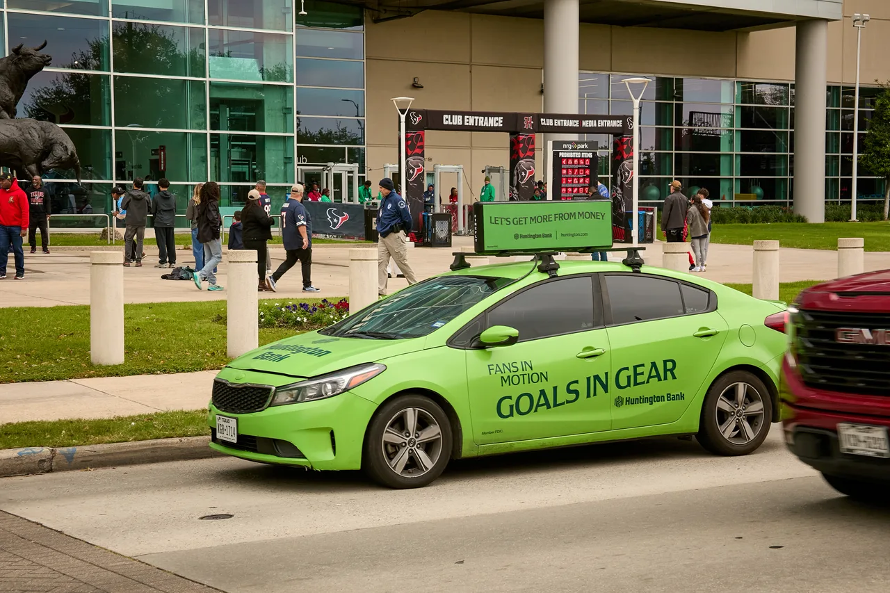 Huntington Bank campaign on a full vehicle wrap carrying a digital top at NRG Park club entrance, Texans game day, Houston, 2025